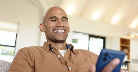 Laughing African American Man Holding Smartphone on Sofa Casual Home Lifestyle