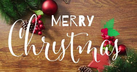 Hand-lettered merry christmas on rustic wood tabletop with evergreen and red ornaments