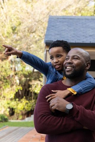 African american father carrying son on back pointing toward distance on backyard deck