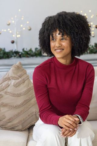 African american woman relaxing on sofa in maroon sweater with cozy festive bokeh lights