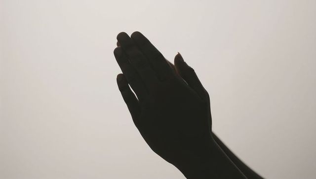 Backlit silhouette hands pressing together in prayer gesture minimal monochrome study
