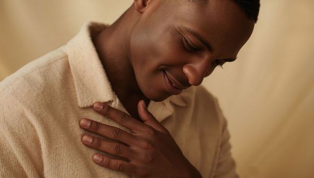 Smiling man wearing cream-beige textured collared sweater, hand on chest, warm closeup