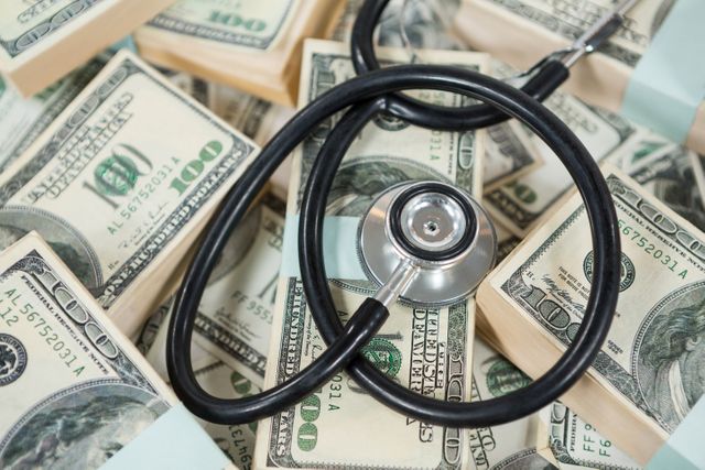 Stethoscope resting on a large pile of US dollar bills, symbolizing the intersection of healthcare and finance. Useful for illustrating concepts related to medical expenses, healthcare costs, insurance, financial health, and economic aspects of the healthcare industry.