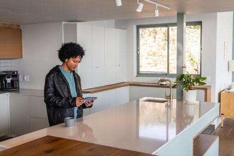 African american man checking tablet at modern kitchen island with coffee mug and plant