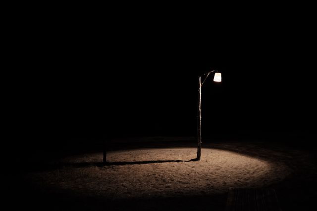 Single lamp post illuminating a small area in the dark night, creating an atmosphere of solitude and isolation. Useful for concepts like loneliness, serenity, or minimalism. Ideal for use in blog posts, mood boards, or social media to convey emotions or evoke thought.