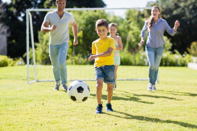 Happy family playing football together outdoors on a sunny day. Parents and children having fun and bonding while engaging in physical activity. Suitable for themes of family, recreation, outdoor activities, and sports.