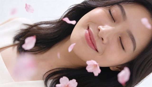 Reclining asian woman smiling with eyes closed surrounded by falling pink blossom petals