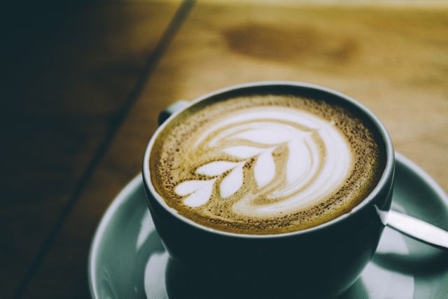 This image captures a close-up view of a latte with intricate frothy milk art in a ceramic cup. Ideal for use in cafe promotions, coffee shop menus, food blogs, social media posts about coffee culture, or advertisements for barista skills and coffee-making workshops.