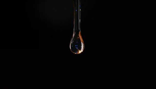 Suspending clear glass droplet with blue and amber reflections against deep black backdrop