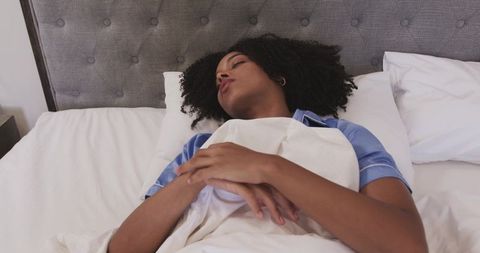 African american woman sleeping peacefully in tufted gray headboard bed with white linens
