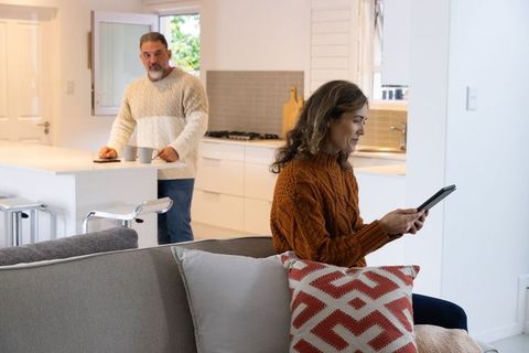 Couple relaxing in modern open-plan home, woman using tablet while man holds coffee mugs