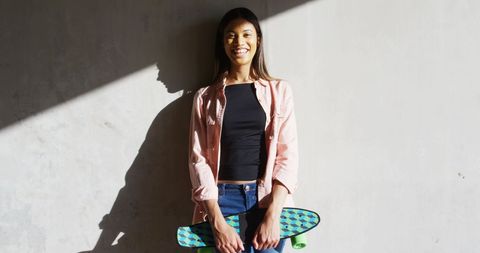 Smiling Woman Holding Skateboard on Sunny Urban Street