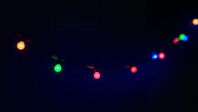 Glowing multicolor globe led string lights arcing across dark night with soft bokeh ambience