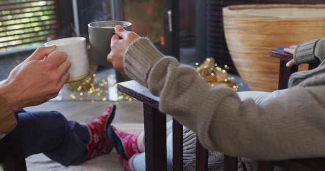 Depicts two people indoors on a winter evening, relaxing with hot drinks wearing sweaters and cozy socks. Ideal for illustrating warmth and comfort during cold seasons, relaxation concepts, or promoting winter-themed products.