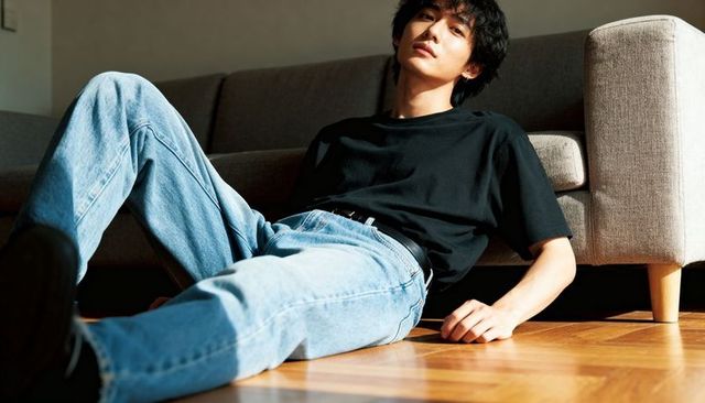 Relaxed young asian man reclining on floor leaning against sofa in sunlit modern living room
