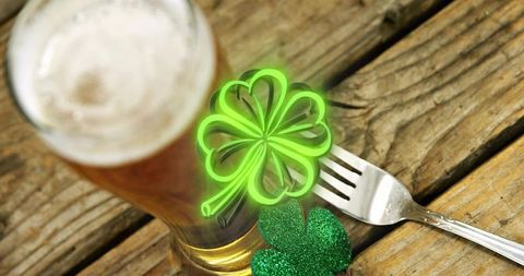 St patrick's day pint of amber beer celebrating with neon clover and rustic wooden table