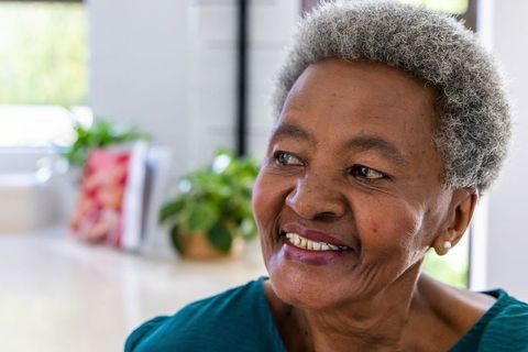 Senior african woman smiling and looking away in sunlit kitchen with pearl earrings