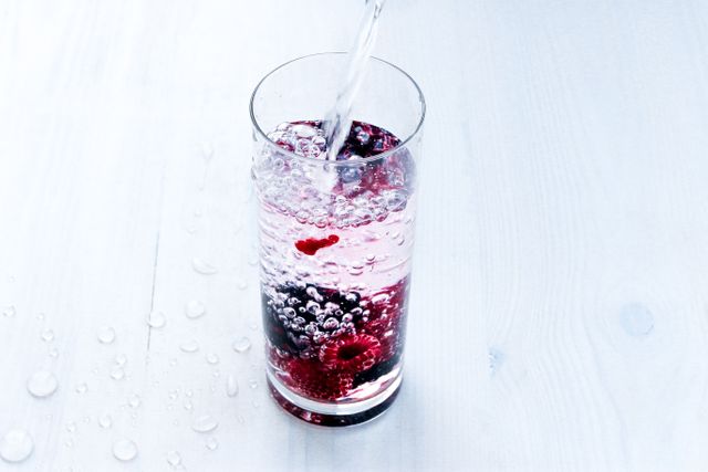 Refreshing sparkling water poured into glass with berries on wooden table. Ideal for illustrating health, hydration, and refreshing summer beverages. Perfect for advertisements, blogs, and articles on healthy drinks and nutrition.