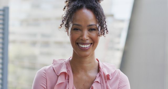 Young professional woman with curly hair smiling confidently while standing outdoors in business attire. The modern urban background creates a professional vibe. Perfect for use in articles, presentations, and promotional materials focused on career success, professional confidence, business environments, and diversity in the workplace.