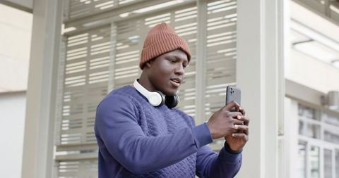 African American Man Using Smartphone under Urban Canopy Wearing Beanie and Headphones