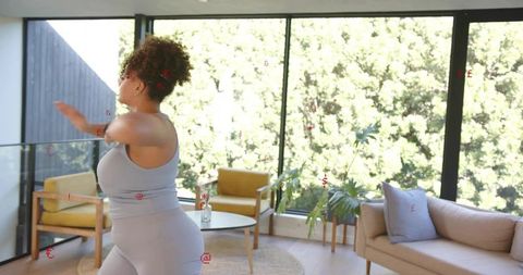 Plus size woman stretching in light gray activewear reaching toward sunlit home interior