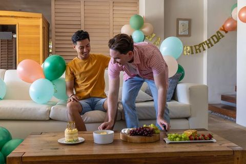Friends celebrating intimate birthday at home with balloons, cake and fruit platter
