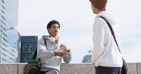 Students talking on city rooftop ledge wearing hoodies and headphones