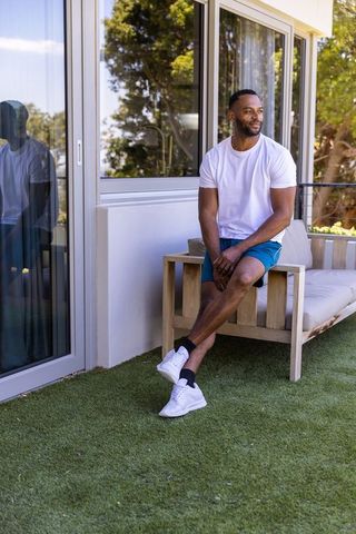 Mature african american man relaxing on balcony bench wearing white t-shirt and sneakers