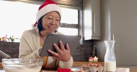 Senior woman baking cookies with tablet guidance during christmas