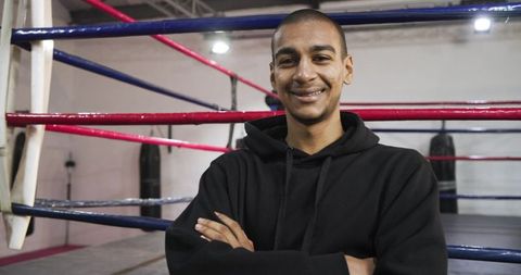 Confident young boxer standing in ring arms crossed flashing smile boxing gym portrait