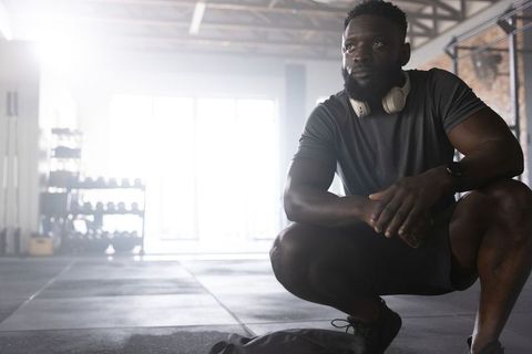 African american athlete resting in industrial gym with headphones, backlit