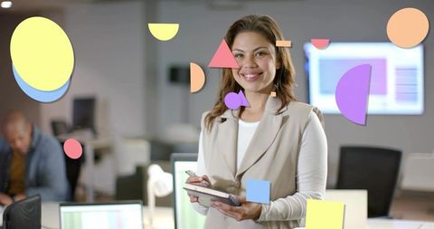 Smiling businesswoman holding tablet with stylus in open office with colorful geometric graphics