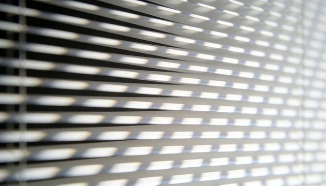 Venetian blinds casting diagonal light and shadow pattern across interior window slats