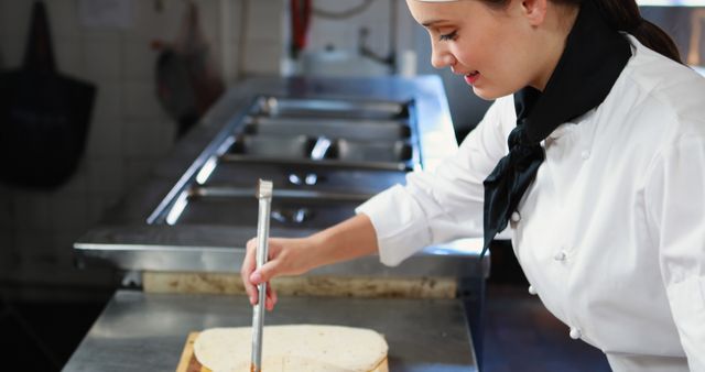 Professional chef is wearing white uniform and black neckerchief, brushing a sauce on a tortilla in a commercial kitchen. Ideal for content related to culinary arts, professional cooking, restaurant businesses, and food industry tutorials.