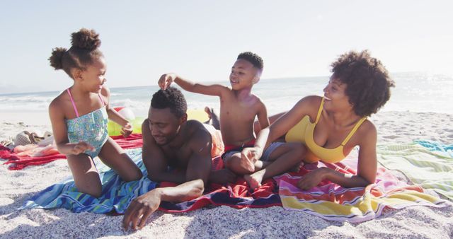 Smiling african american family lying on towels on sunny beach. healthy, active family beach holiday.
