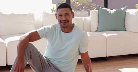 Man in comfortable sportswear relaxing on yoga mat in sunlit living room