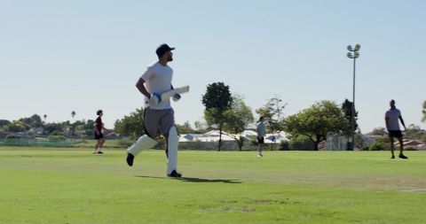 Batsman running between wickets wearing pads gloves cap on sunny suburban cricket pitch