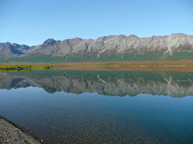 Beautiful rocky mountain range perfectly reflected in calm lake on clear day. Captures natural beauty and tranquility of wilderness, ideal for environmental campaigns, travel promotions, nature-inspired designs, and peaceful settings for backgrounds.