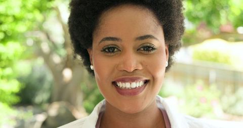 Smiling Woman in Garden with Pearl Earrings Symbolizing Natural Elegance