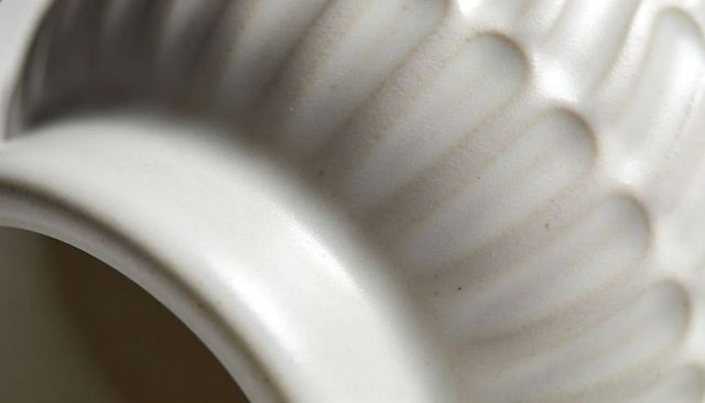 Close-up showing off-white glazed ceramic vessel with scalloped fluting, rim, inner cavity