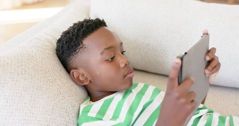African american boy reclining on sofa using tablet for calm focused learning at home