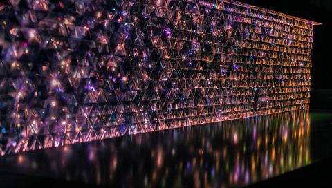 Glowing prism wall with multicolor led refractions and black floor reflections, triangular modules