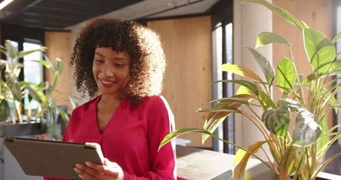 Professional Woman Reviewing Tablet in Modern Office with Greenery and Natural Light