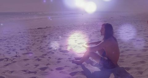 Man sitting on beach watching horizon at sunset, spiritual reflection