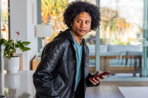 Young african american man turning head holding smartphone in modern home