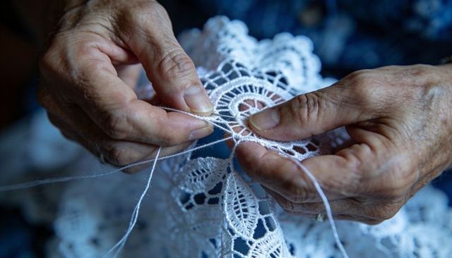 Senior hands stitching intricate white lace doily with fine thread and shuttle