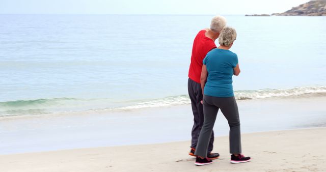 Senior couple walking on the beach, watching the ocean. Ideal for themes on senior living, healthy lifestyle, spending time together, retirement relaxation, travel, and peaceful moments by the sea. Perfect for newsletters, health and wellness articles, travel brochures.
