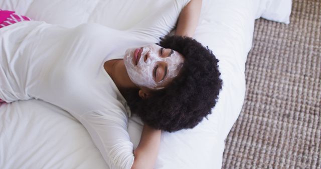 Woman taking a break and enjoying a face mask treatment while lying on her bed. Ideal for advertisements and content related to skincare, health and wellness, beauty routines, and self-care practices.
