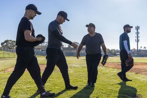 Baseball teammates walking across sunlit outfield wearing caps and holding gloves