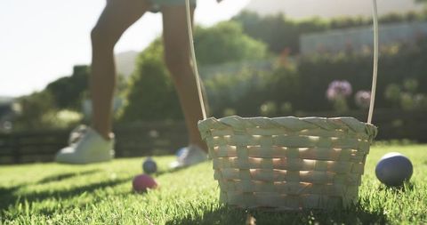 Backlit easter basket on sunlit lawn with youth stepping past colorful eggs